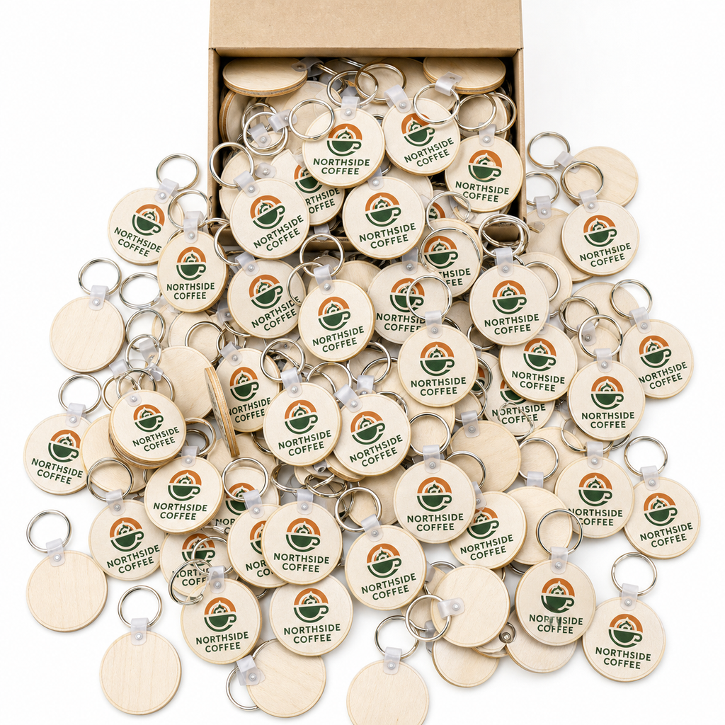 Large bulk quantity of round wood keychains printed with a coffee shop logo, tipped out of a kraft box
