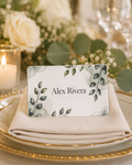 Custom acrylic place card, greenery design with guest name in full color, on a folded napkin at an elegant wedding place setting